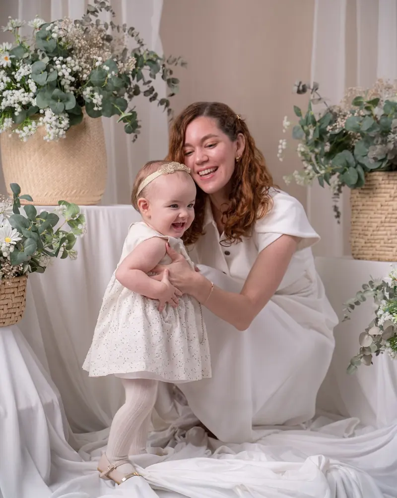 Mamá con su bebé de un año en un set de flores blancas